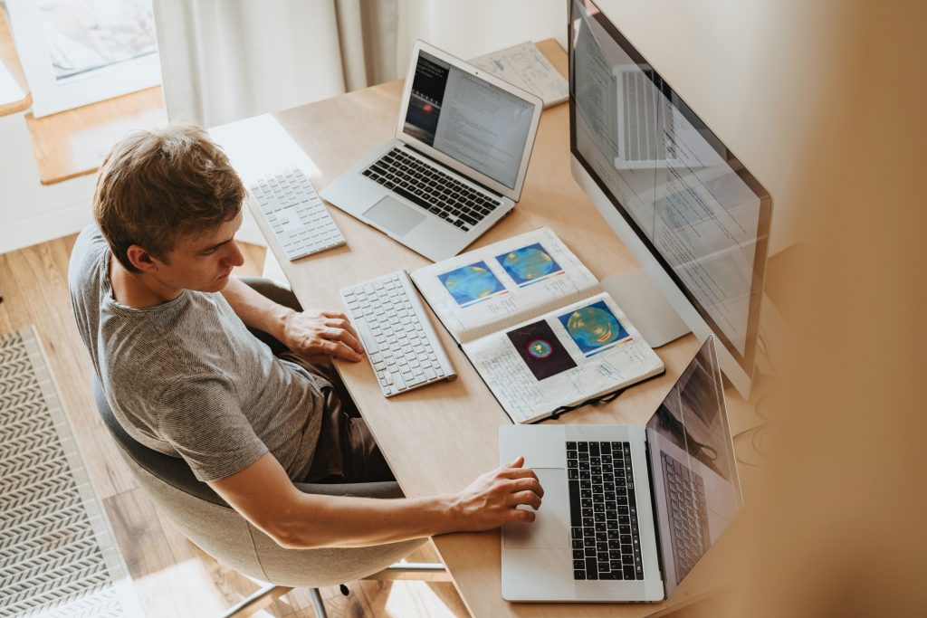 Person mit mehreren Laptops und einem Monitor vor sich.