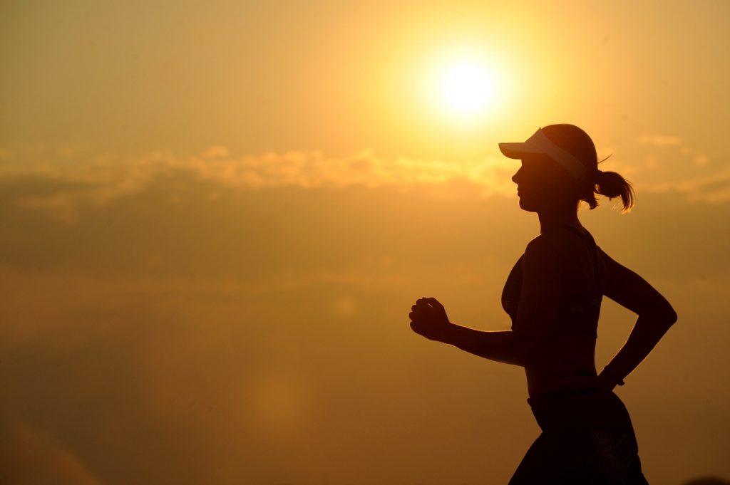 Frau joggt mit dem Sonnenuntergang im Hintergrund.